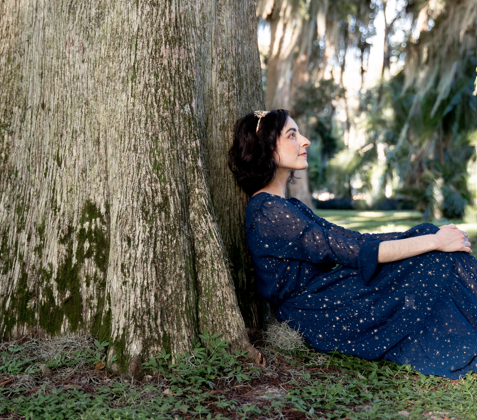 Woman in dark blue dress sitting and leaning against a tree
